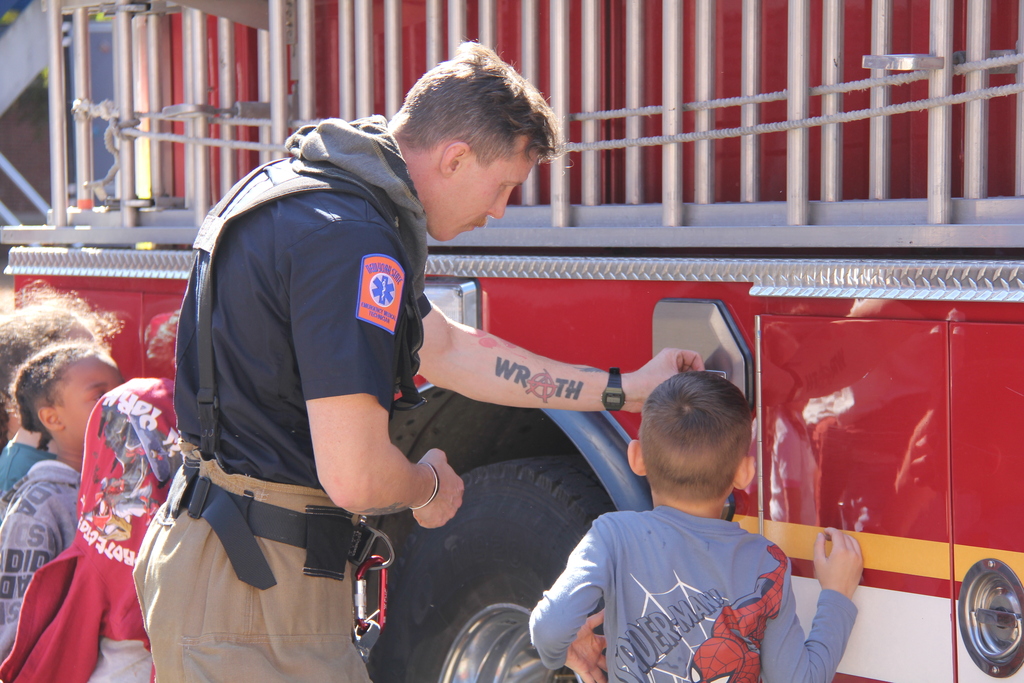 A firefighter with a watch on his arm shows a child how to open a fire truck door.