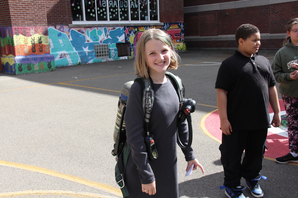 A girl poses for a photo with a fire fighter pack on her back