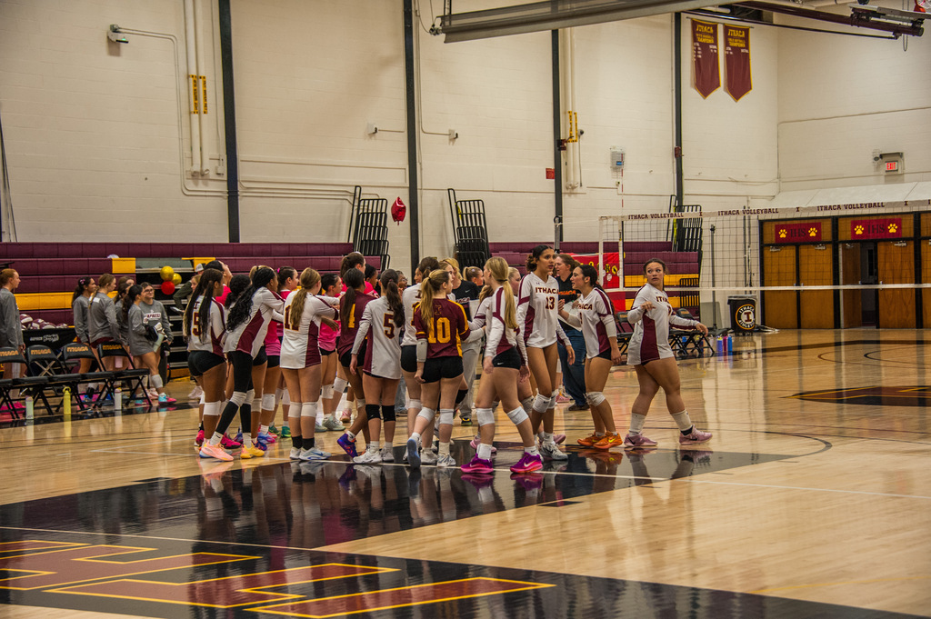 Group of volleyball players standing in a circle with a volleyball net in the background.