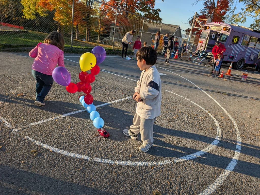 Two children stand by a large balloon sculpture while others walk around a parking lot.