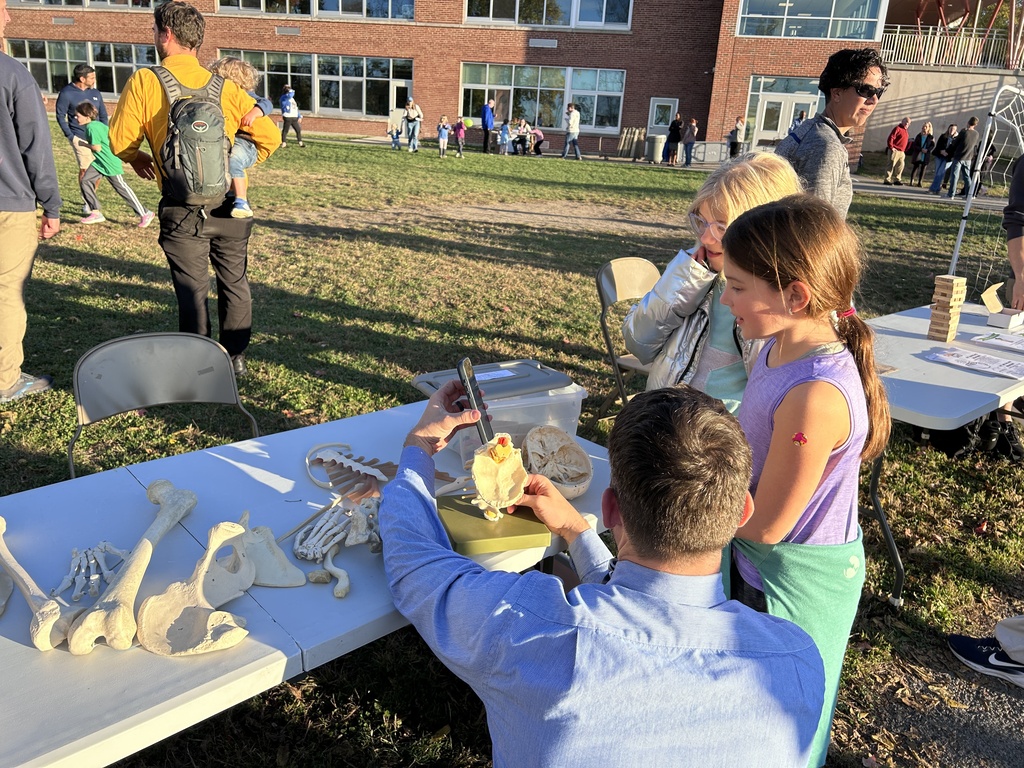 A group of students at tables with various fossils. A man uses a tool on an item.