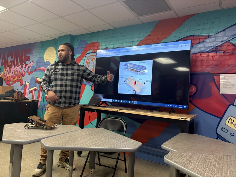 Akil presenting in front of a monitor at the front of a classroom
