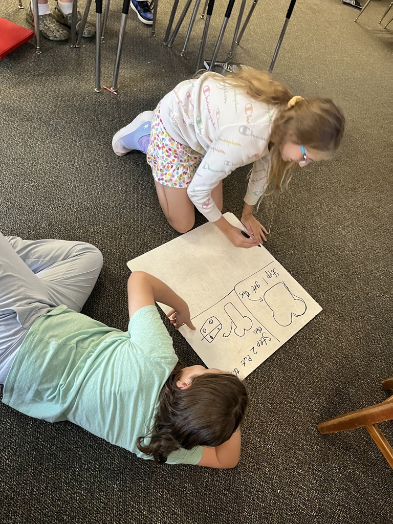 Students sit on the floor as they work on a whiteboard modeling how to make toast.