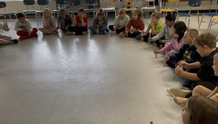 students sitting in a circle passing sticks around.