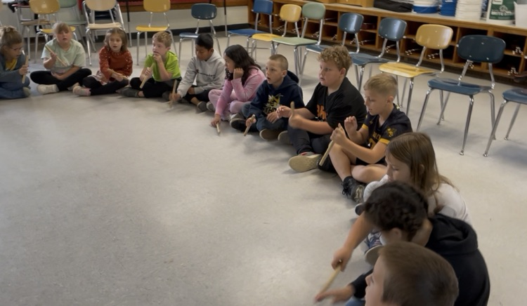 students sitting in a circle passing sticks around.