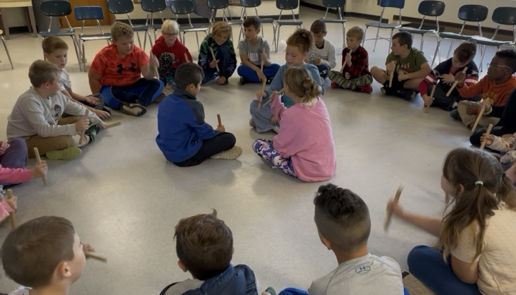 students sitting in a circle passing sticks around.