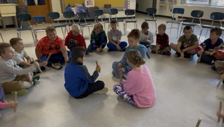 students sitting in a circle passing sticks around.