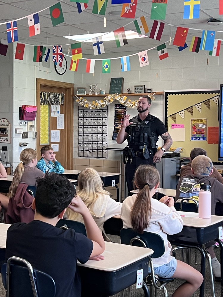 Officer Greene in uniform speaking to 6th-grade students seated at desks in a classroom.