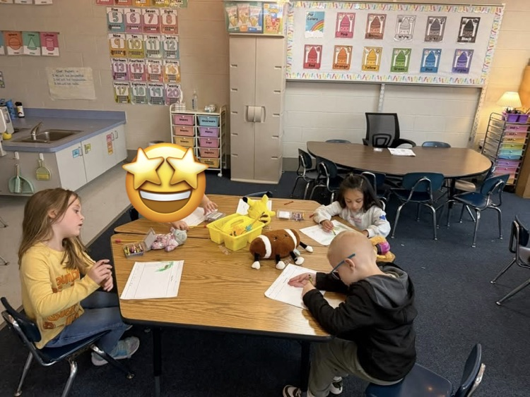 students at a table doing work with their stuffies