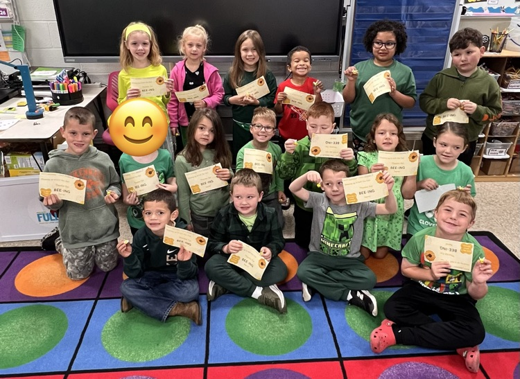 Students sitting on the carpet with awards.