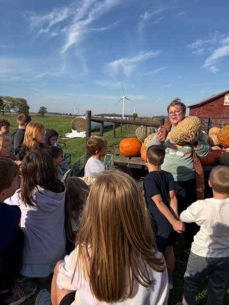 adult holding a pumpkin in front of children