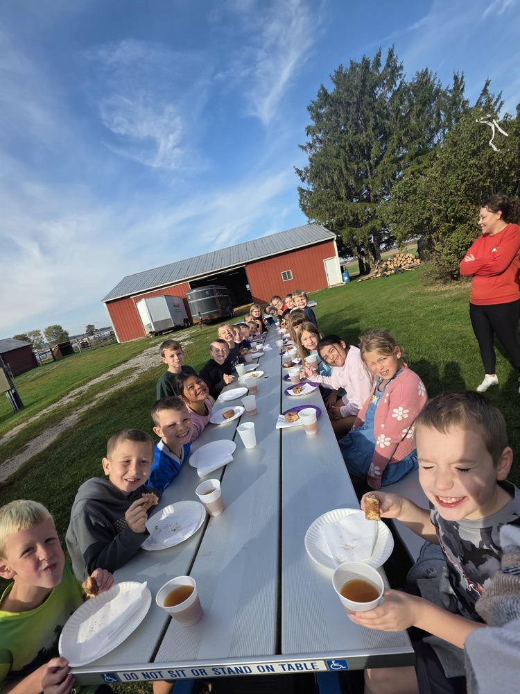 Students sitting at a large table with cider and donuts.