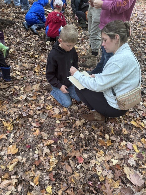 Student and adult looking at leaves in the woods.