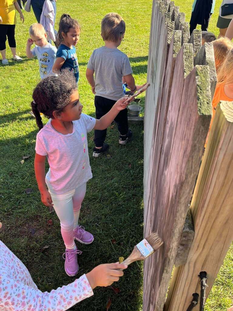 Students use water to pretend to paint a fence.