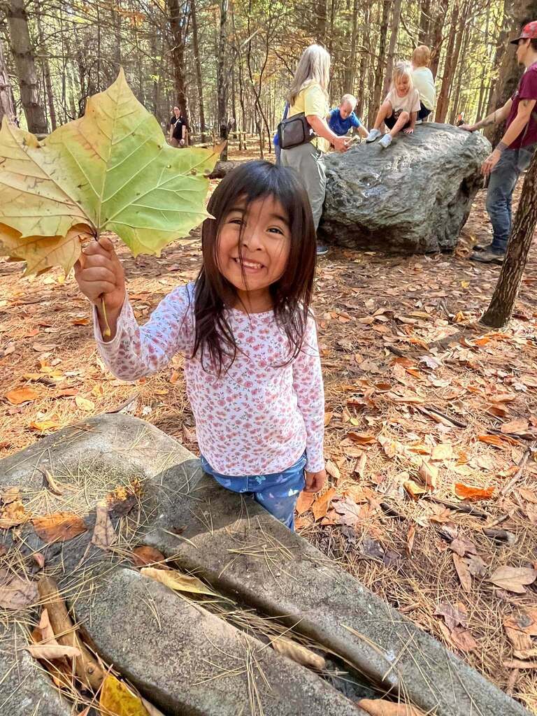 A student holds a large leaf while smiling.
