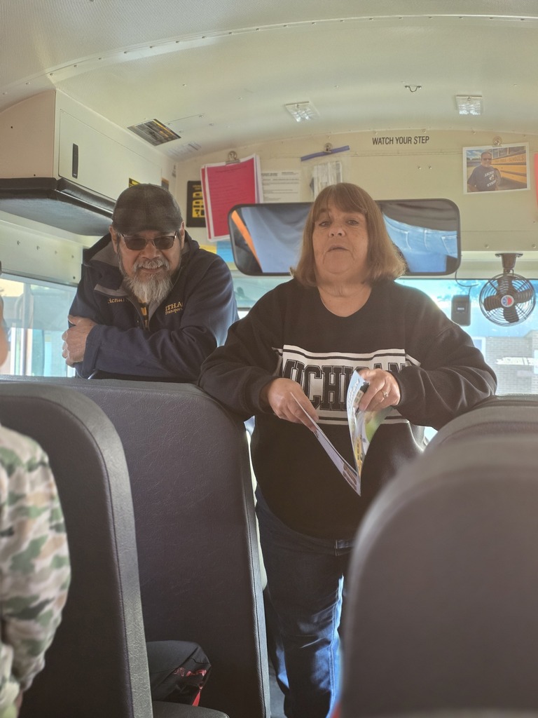 Two bus drivers talking with students inside a school bus.