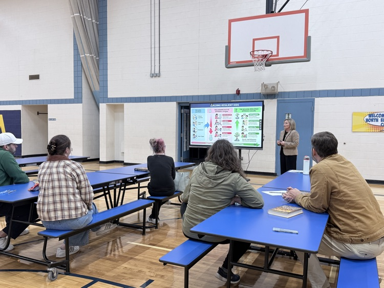 parents watching a presentation while seated at tables.