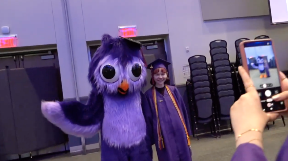 owl mascot standing with a student in a graduation cap and gown
