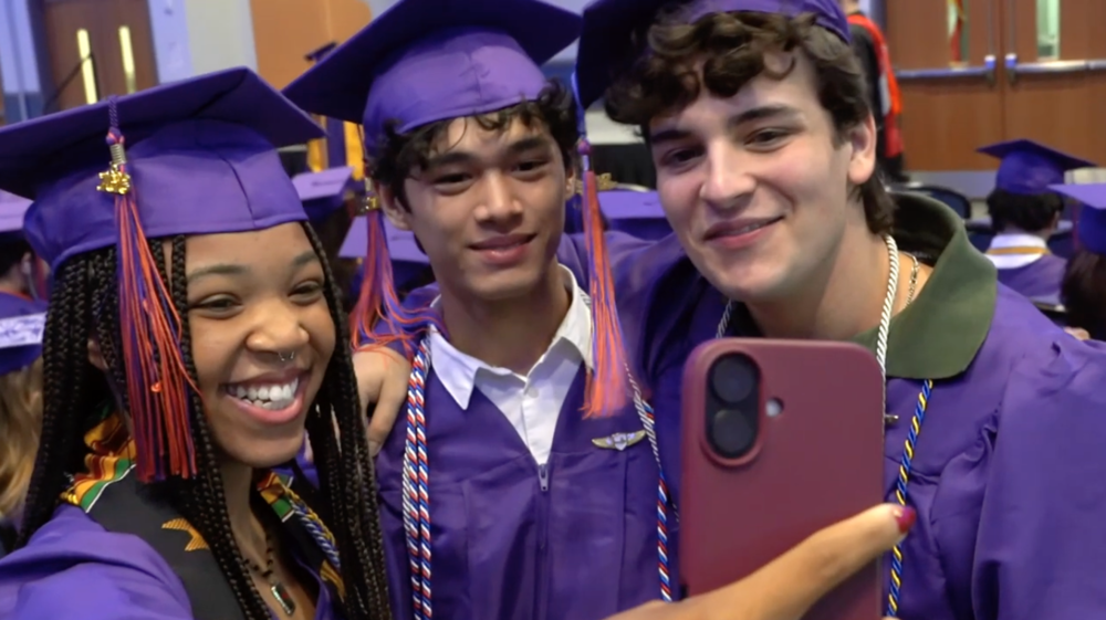 three students in purple graduation caps smiling for a slefie