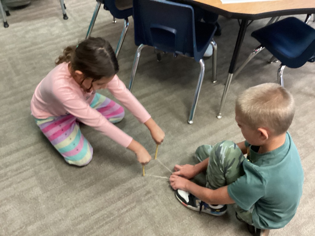 Two students are performing an experiment with marbles and a rubber bands.