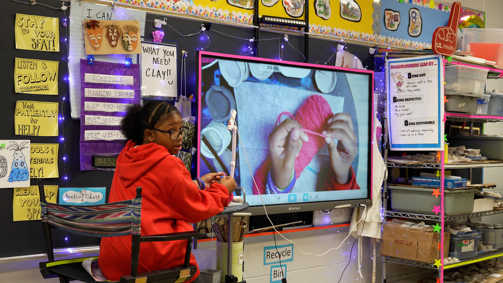 Girl looking towards a class while demonstrating how to crochet