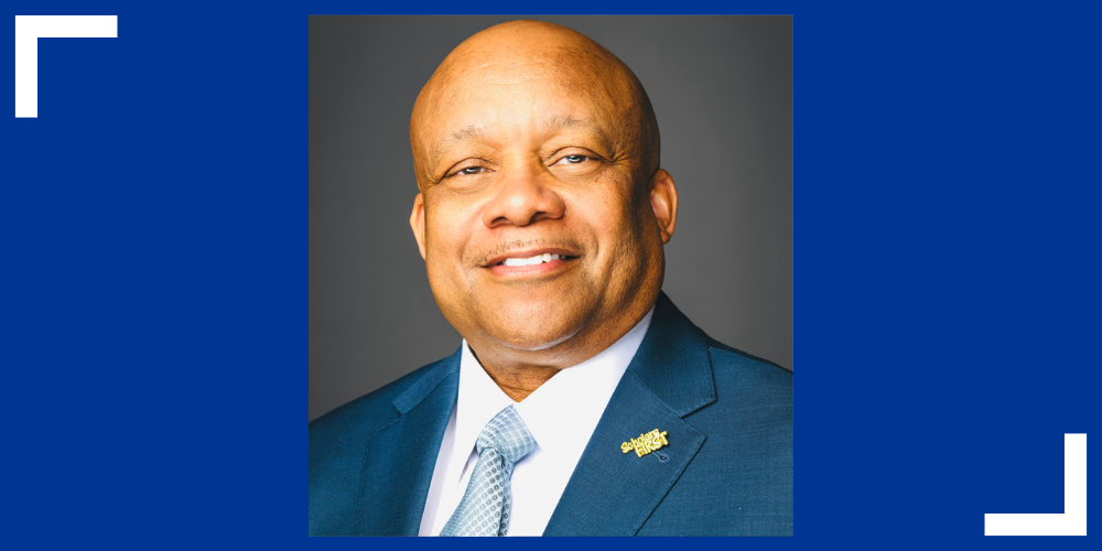 Dr. Brian Yearwood smiling in a blue suit jacket, white shirt, and blue tie.
