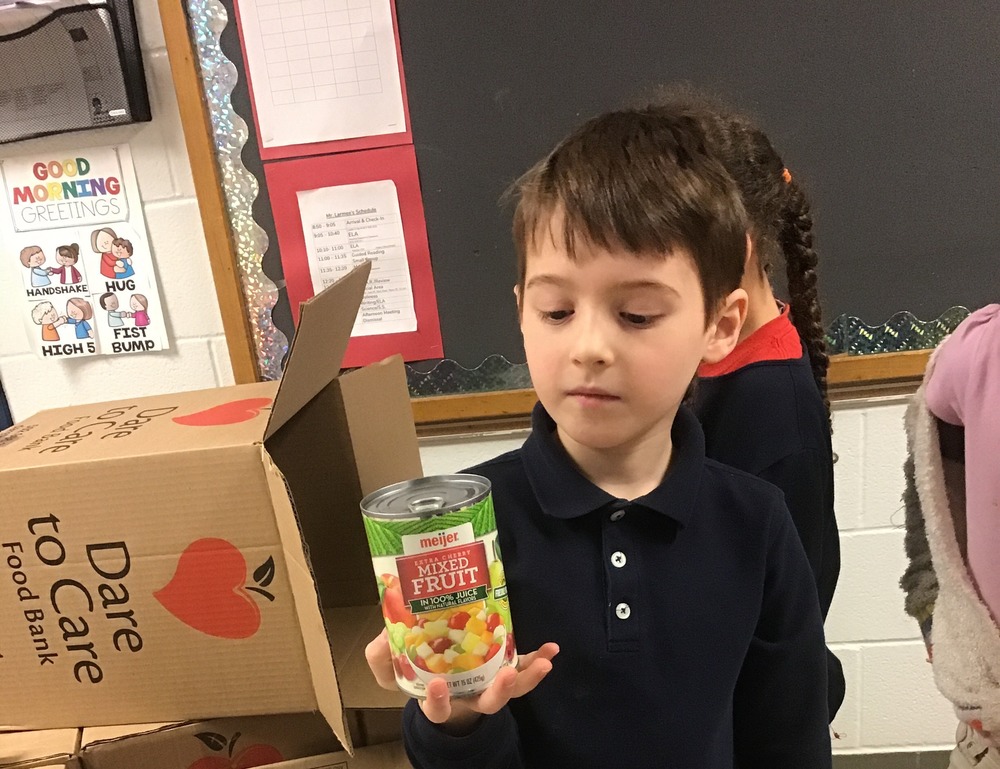 Student holding can of fruit infront of Dare to Care Food Bank Box