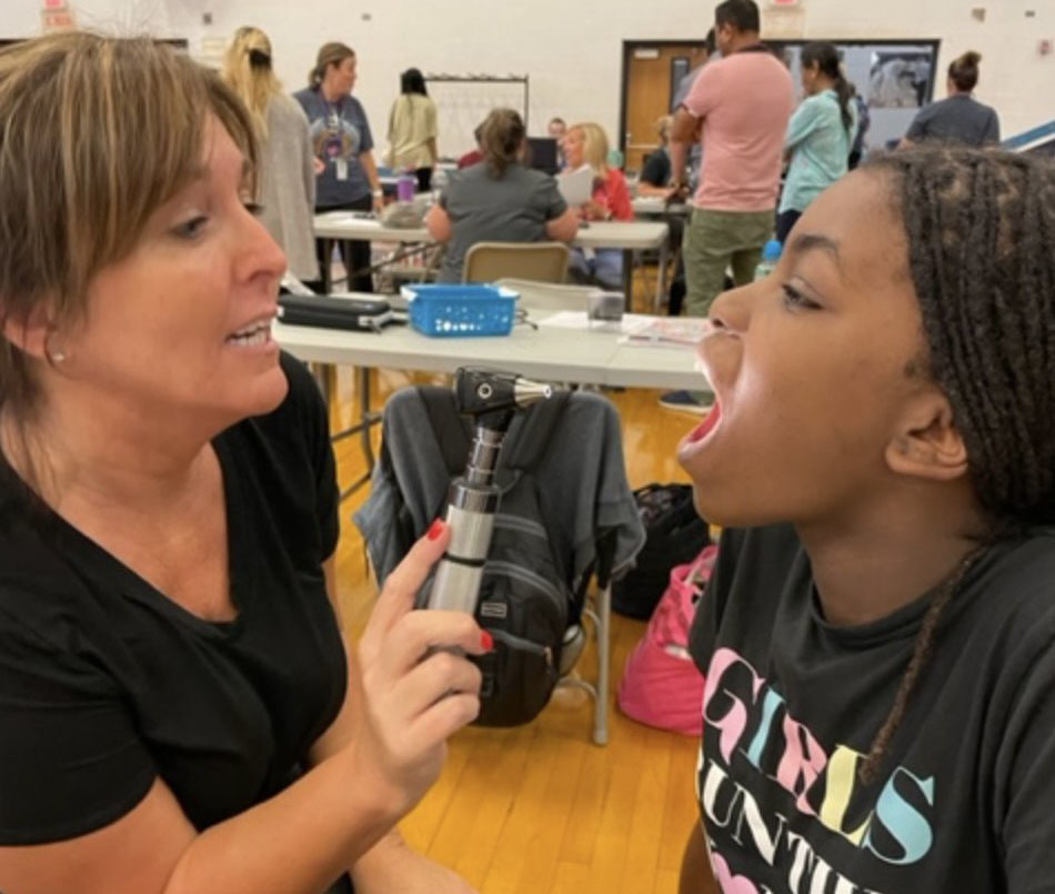 A school nurse looks in a student's mouth during a physical exam.