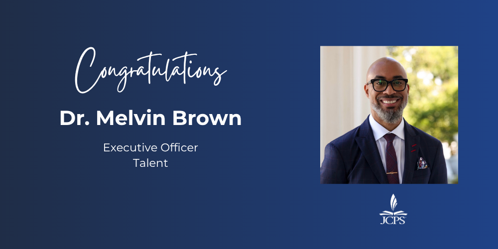 A graphic on a dark blue background that reads "Congratulations Dr. Melvin Brown, Executive Officer, Talent." Below the text is a square photograph of Dr. Brown, a smiling Black man with a shaved head, beard, and glasses, wearing a navy suit, white shirt, and tie. At the bottom center is the white logo for JCPS.
