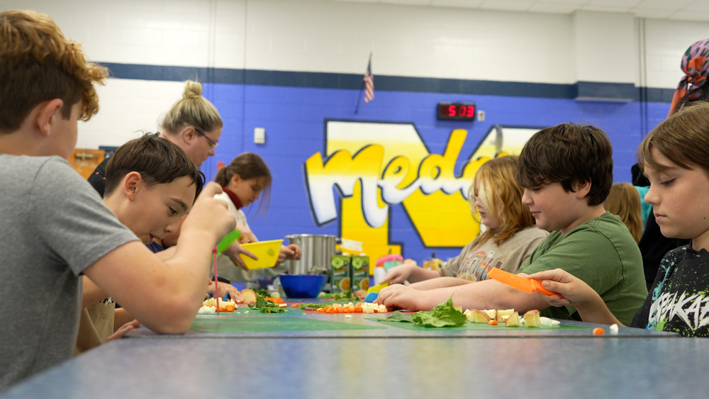 Students sitting at a table cutting vegetables 