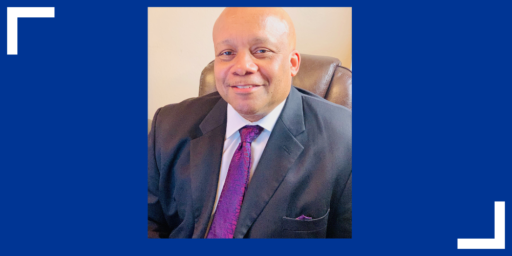 Dr. Brian Yearwood sitting in a chair with a purple tie and black suit jacket