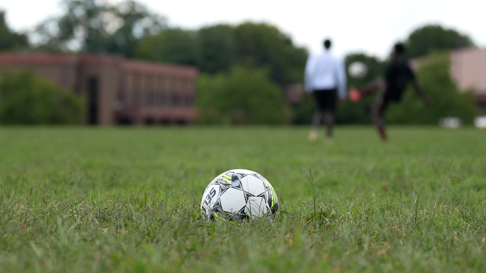 Soccer ball in the foreground with a boy kicking it in the background