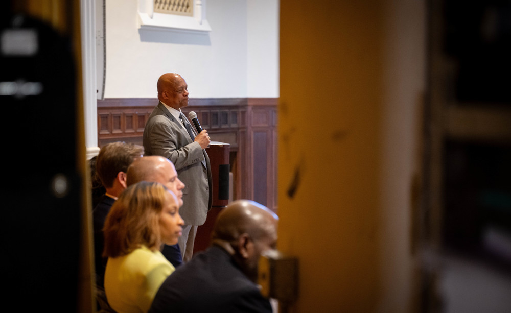 Dr. Brian Yearwood on stage, holding a microphone while members of his leadership team look to the audience.