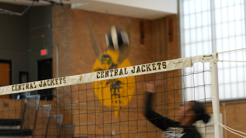 Volleyball net that says "Central Jackets" on it with a volleyball player about to hit the ball