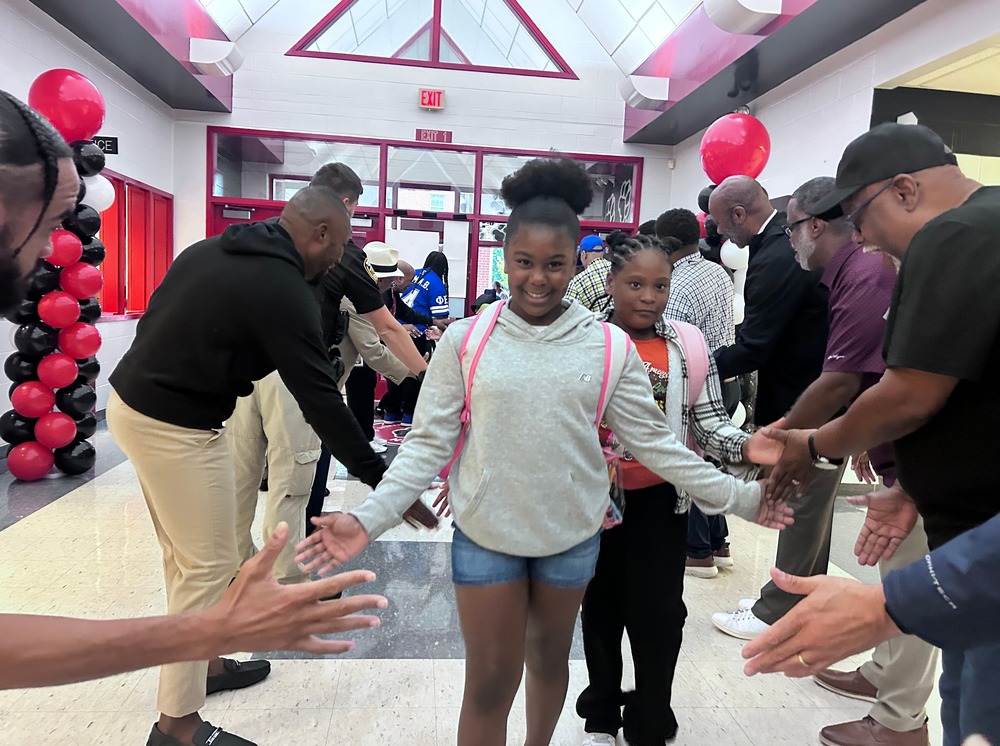 Maupin Elementary student walks into school with a big smile while high fiving Flash Dads