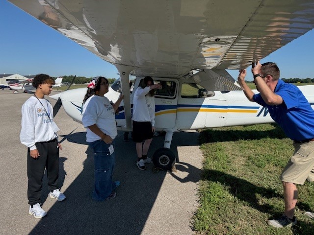 Students looking underneath wing of plane with instructorc