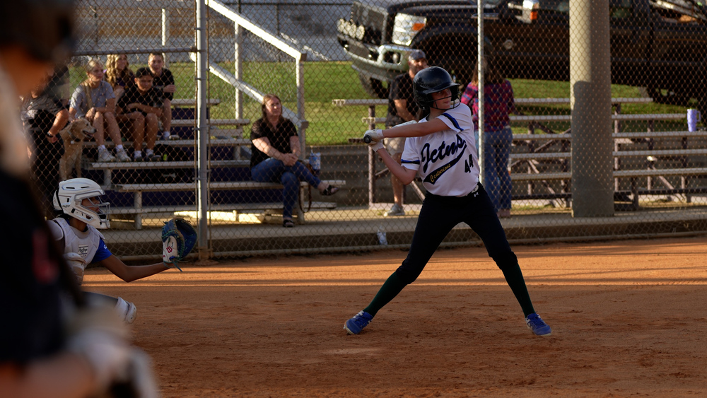 Girl swinging a softball bat, wearing a jersey that says 'JCTMS' on the front