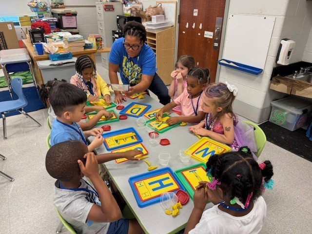 Young students sitting at table doing letters and numbers with teachern