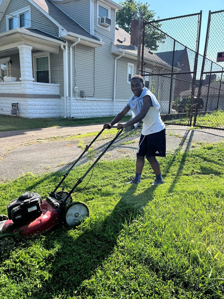 A student pushes a lawn mower over grass.