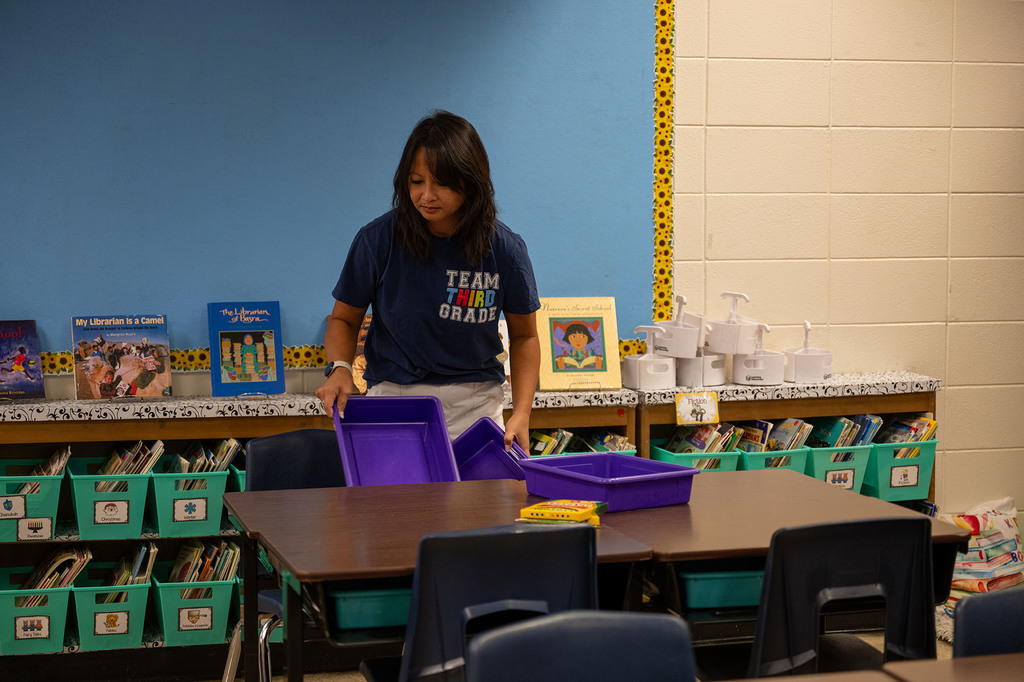 A teacher puts a purple bin in a desk in her classroom.