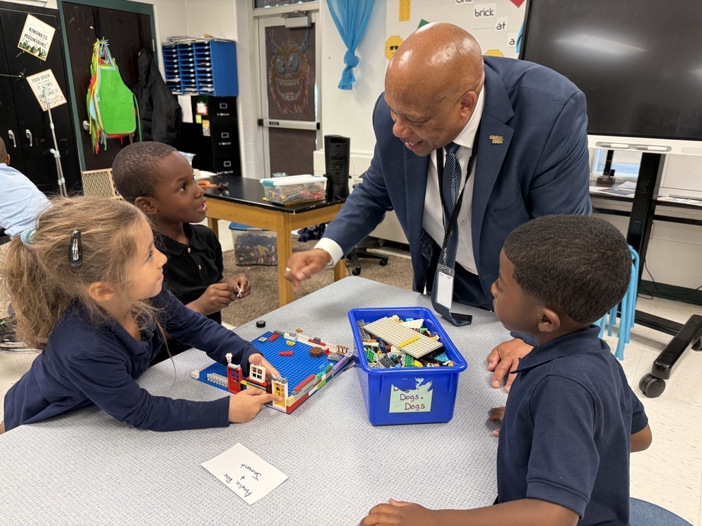 Dr. Yearwood. talks to students who are sitting at a table building with legos.