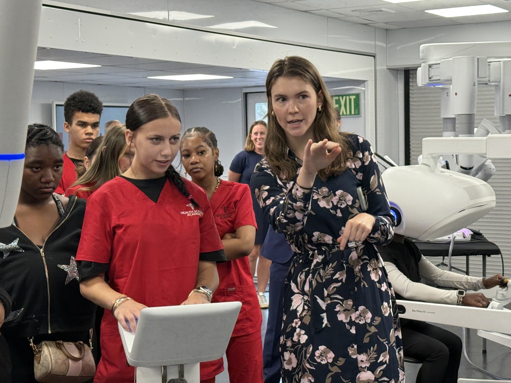 A student operates medical machinery while an adult talks to her.
