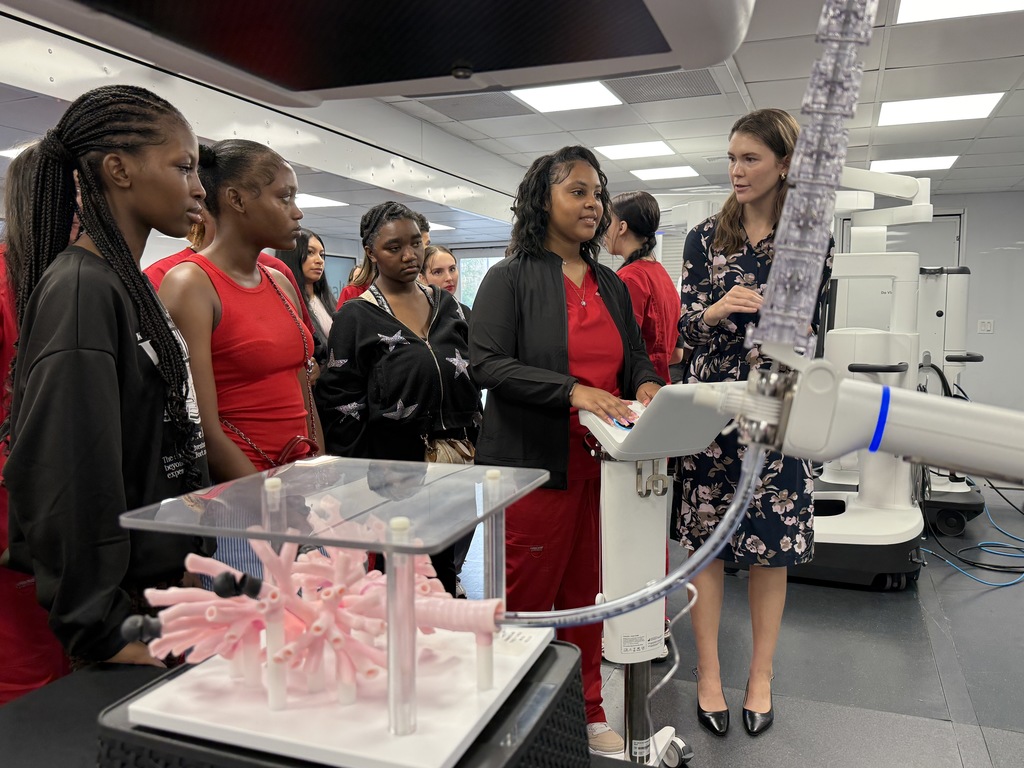 A student operates medical machinery while other students and an adult stand nearby. 