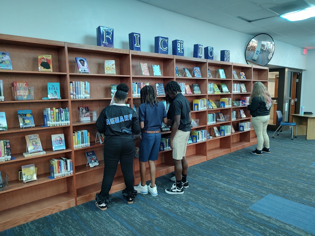Students stand at bookshelves in their school library.