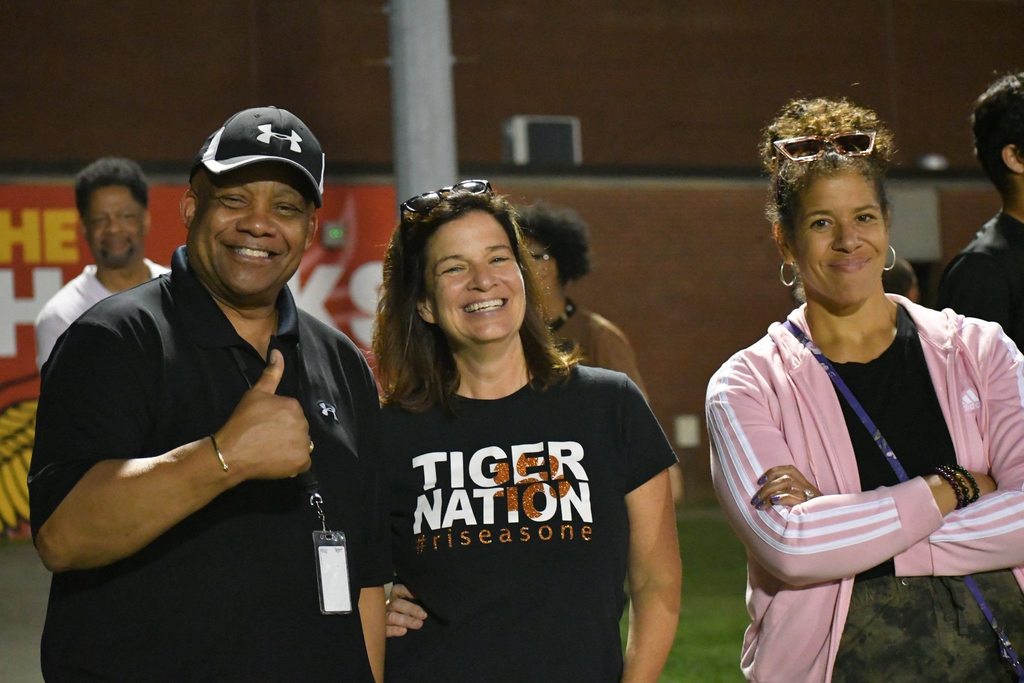 Dr. Yearwood poses for a picture with two JCPS staff members on a football field. 