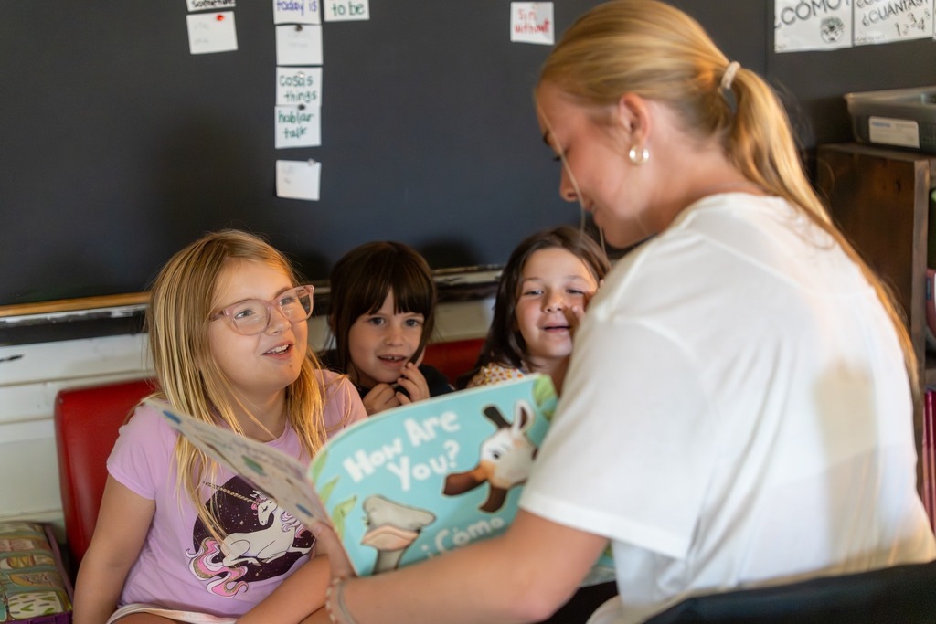 A student reads a book to younger students.