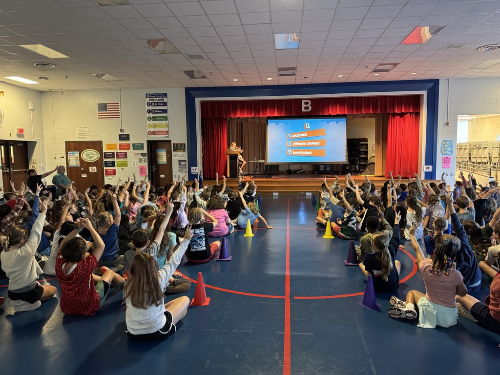 Students raise their hands while sitting on a gym floor.