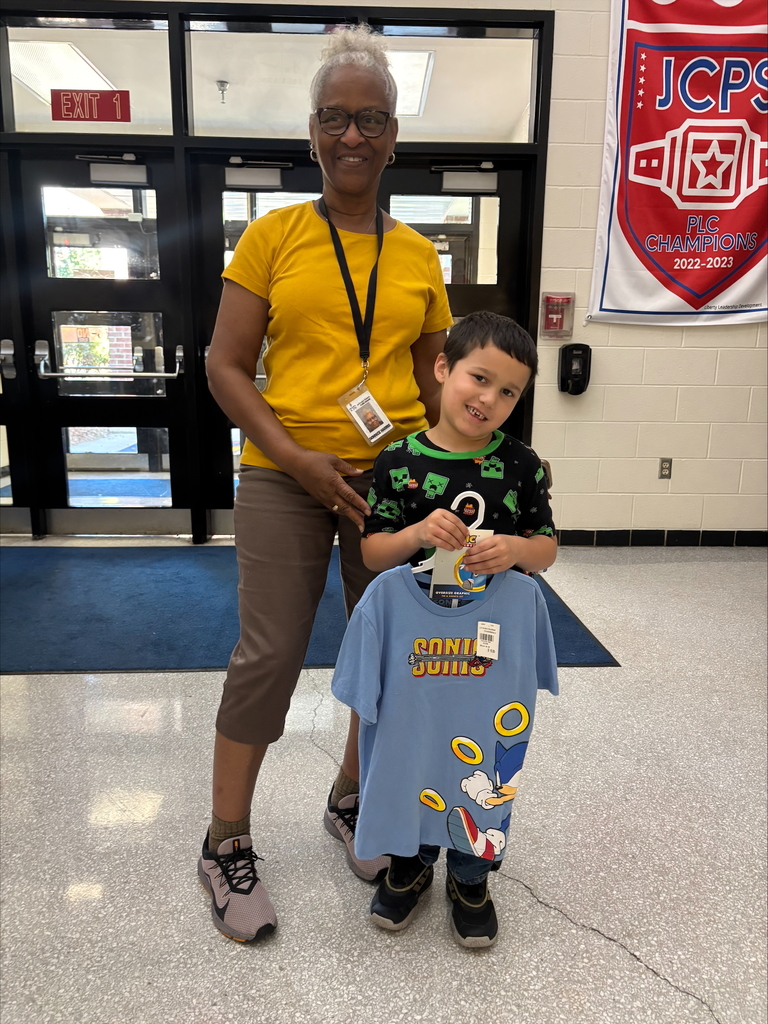 An adult and a student holding pajamas smile for a photo. 