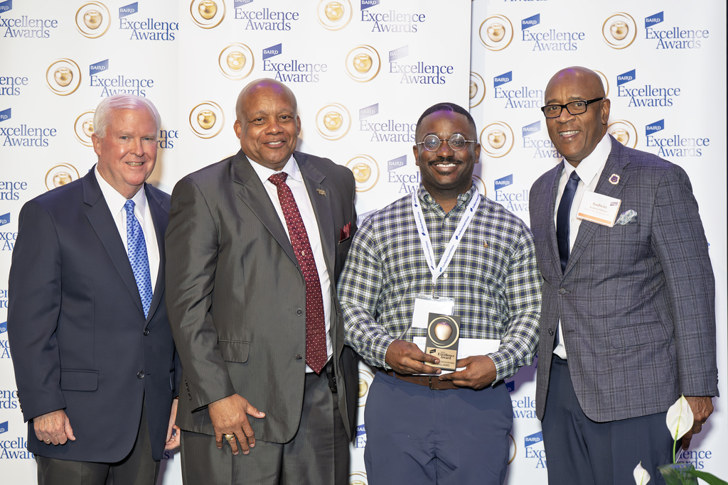 A Baird Award winner poses for a picture with three other adults while holding their award.