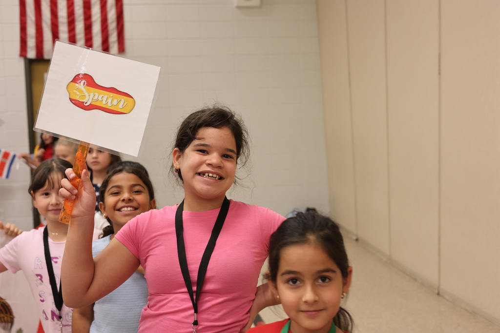 A student holds up a sign that says "Spain" while other students stand nearby and smile.